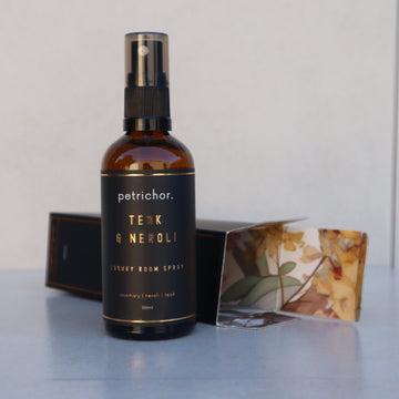 Bottle of petrichor Teak & Neroli Luxury Room Spray on a reflective surface with a neutral background