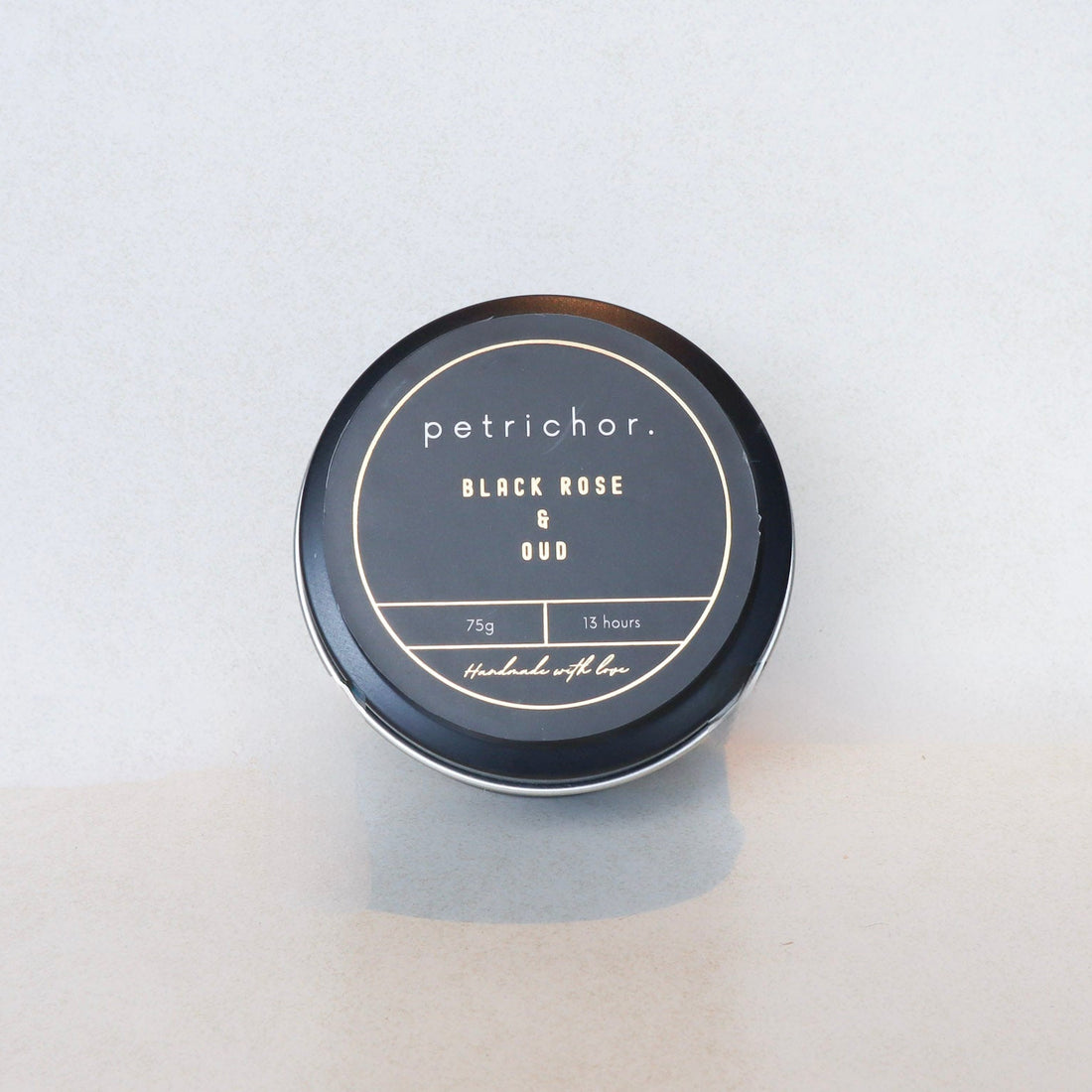 Candle jar labeled 'petrichor. Black Rose & Oud' on a light gray background