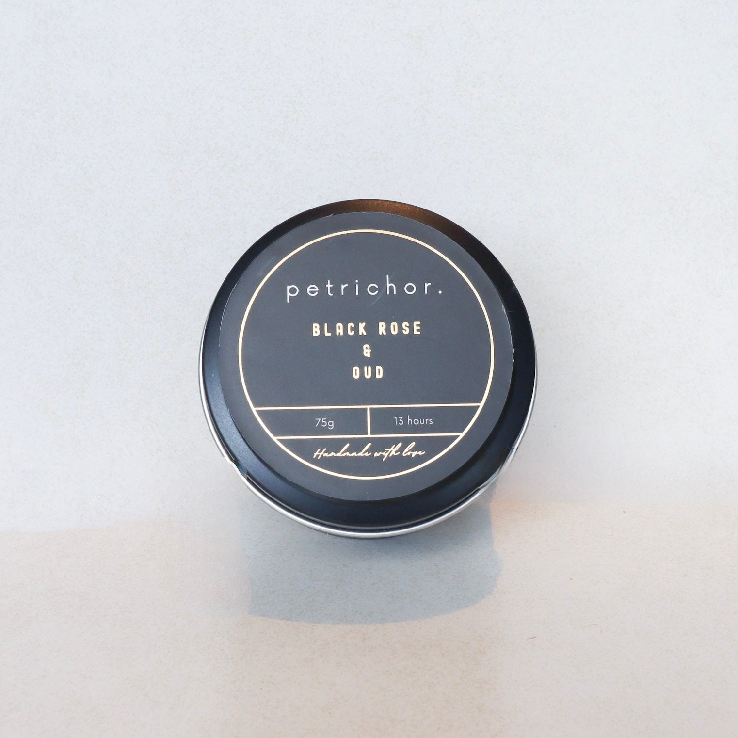 Candle jar labeled 'petrichor. Black Rose & Oud' on a light gray background