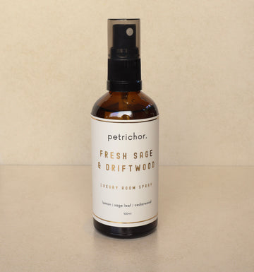 Brown spray bottle labeled 'petrichor' with 'Fresh Sage & Driftwood' on a beige background