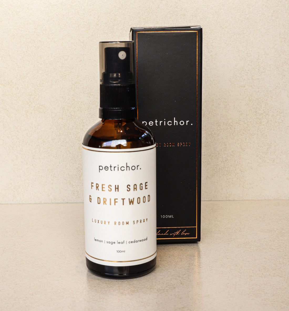 Brown spray bottle labeled 'petrichor' with 'Fresh Sage & Driftwood' on a beige background