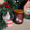 Sugarplum Feast Christmas candle beside a nutcracker snow globe and gingerbread house
