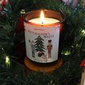 Lit Nutcracker's Waltz Christmas candle with a nutcracker and Christmas tree label, surrounded by fairy lights