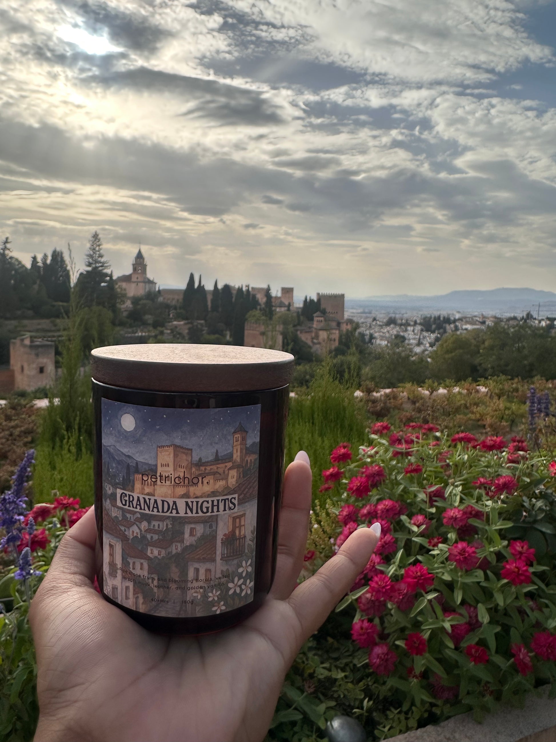Hand holding a candle with a scenic label against a blurred natural background