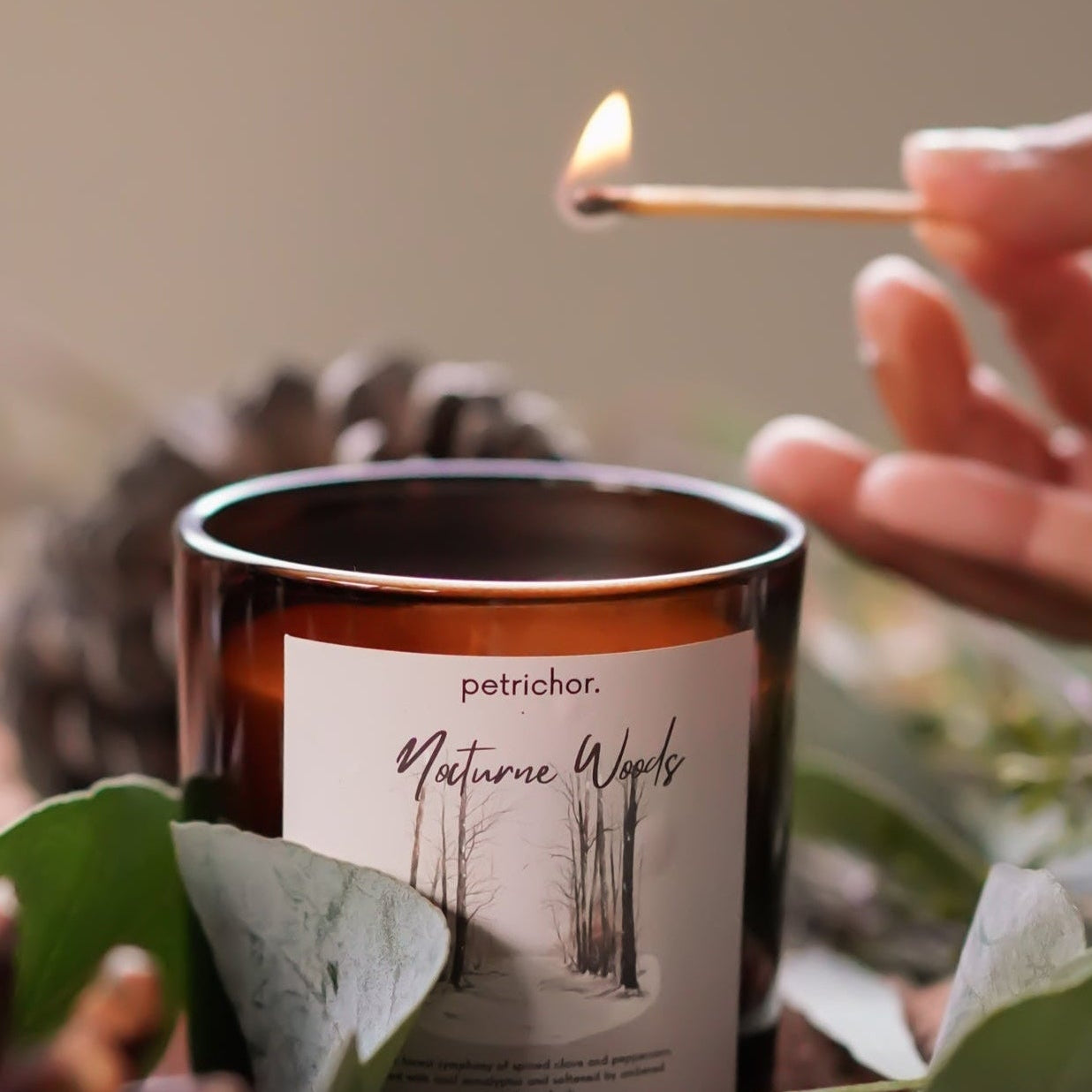 Candle being lit with a match, surrounded by natural elements like leaves and pinecones.
