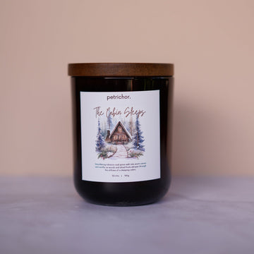 Candle with a label featuring a cabin design on a beige background