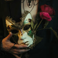 Person holding a decorative mask and red roses against a dark background
