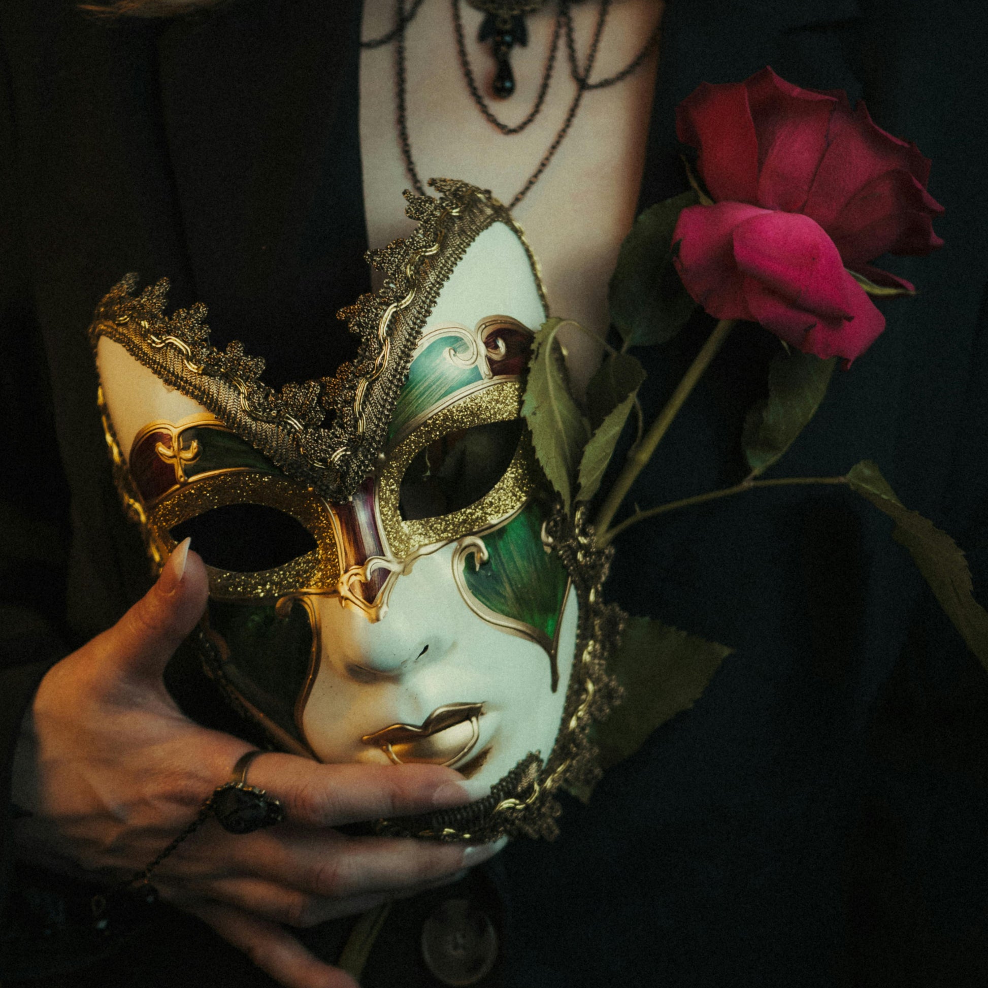 Person holding a decorative mask and red roses against a dark background