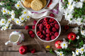 Wooden table with bowl of raspberries, apples, and cookies surrounded by flowers.